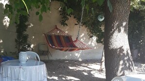 Un espace extérieur aménagé avec une table ronde et des chaises, un hamac suspendu et un arbre qui offre de l’ombre.