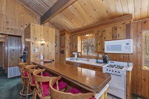 A wooden interior with a kitchen area, bar stools, and a stove.
