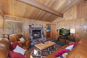 A cozy living room with a fireplace, leather sofas, a television, and wooden paneling.