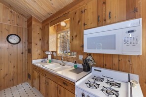 A kitchen with wooden walls, a microwave, a stove, a sink, and a clock.