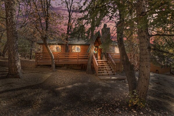 A cabin with a wooden exterior, a staircase leading to the entrance, and surrounded by trees.