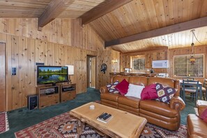 A wooden interior with a leather sofa, a television, and a dining area.