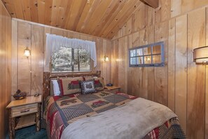 Habitación con paneles de madera, una cama, una mesita de noche, una ventana con vistas e iluminación en la pared.