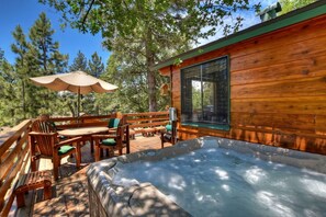 Una cabaña de madera con jacuzzi, mobiliario exterior y un amplio ventanal.