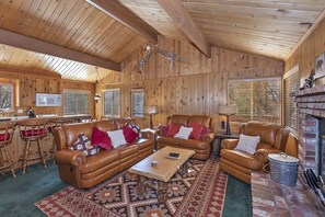 A cozy cabin interior with a wooden interior, leather furniture, a fireplace, and a kitchen area.