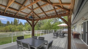 A covered deck with a table and chairs, a hot tub, and a view of a forested area. - Eagle Point Cabin Backing to 7 Acres of Preserve! HOT TUB!  A/C! PET FRIENDLY! Walk to Lake & Shuttles! (Big Bear Lake)