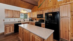 A kitchen with wooden cabinets, a granite countertop, a black refrigerator, and a stove. - Eagle Point Cabin Backing to 7 Acres of Preserve! HOT TUB!  A/C! PET FRIENDLY! Walk to Lake & Shuttles! (Big Bear Lake)