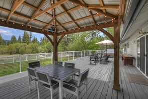 Una terraza cubierta al aire libre con mesa y sillas, una pérgola con luces colgantes y vistas a la vegetación circundante.