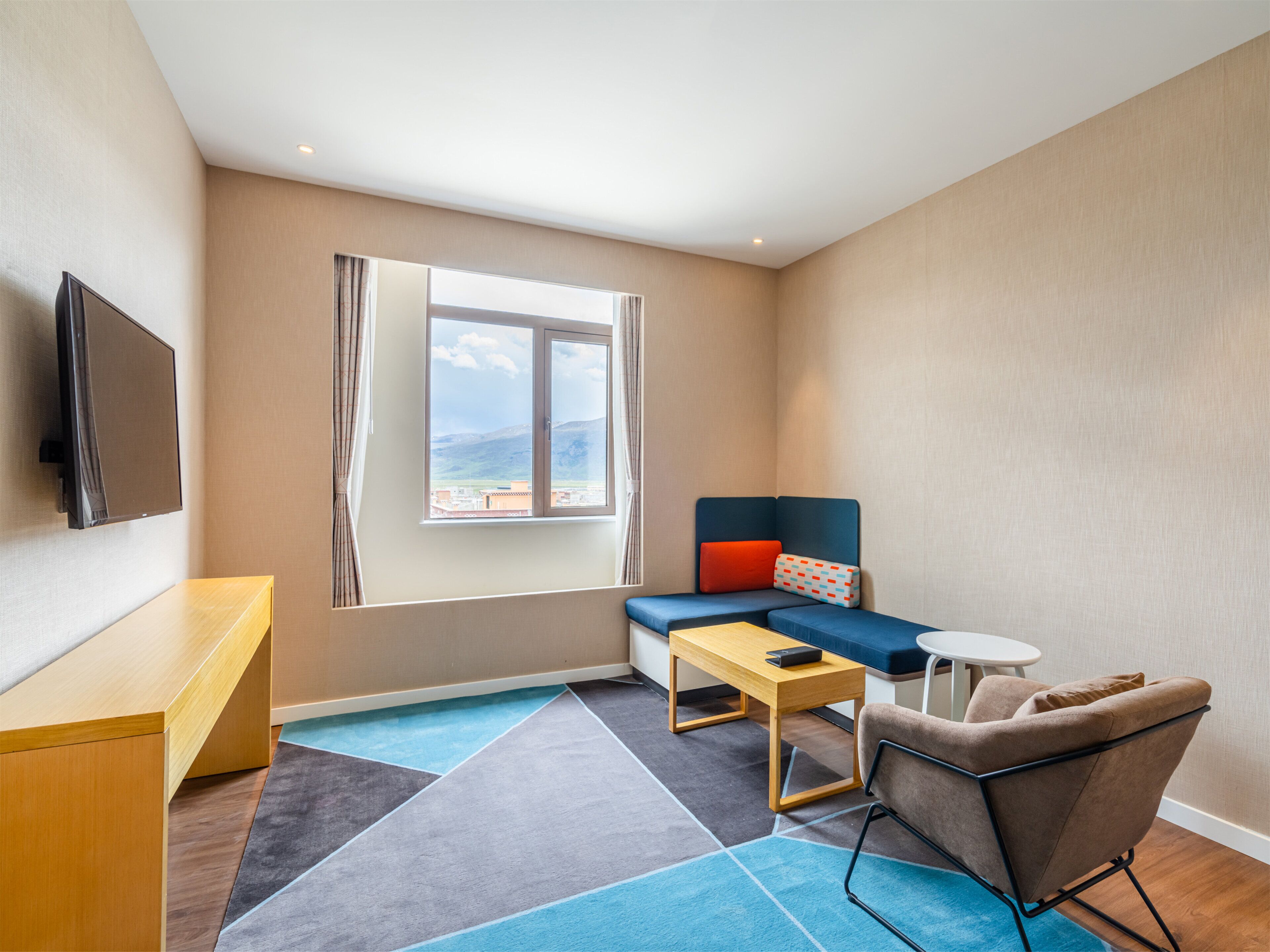 Una habitación de hotel moderna con un ventanal grande, un televisor de pantalla plana, un sofá, una silla y una mesita.