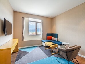 A modern hotel room with a large window, a flat-screen TV, a sofa, a chair, and a small table. - Holiday Inn Express Litang by IHG (Garze)