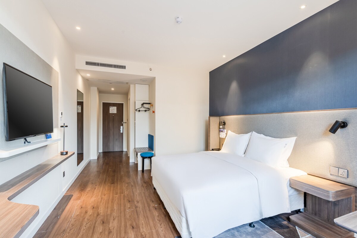A modern hotel room with a large bed, a flat-screen TV, a desk, and a seating area.