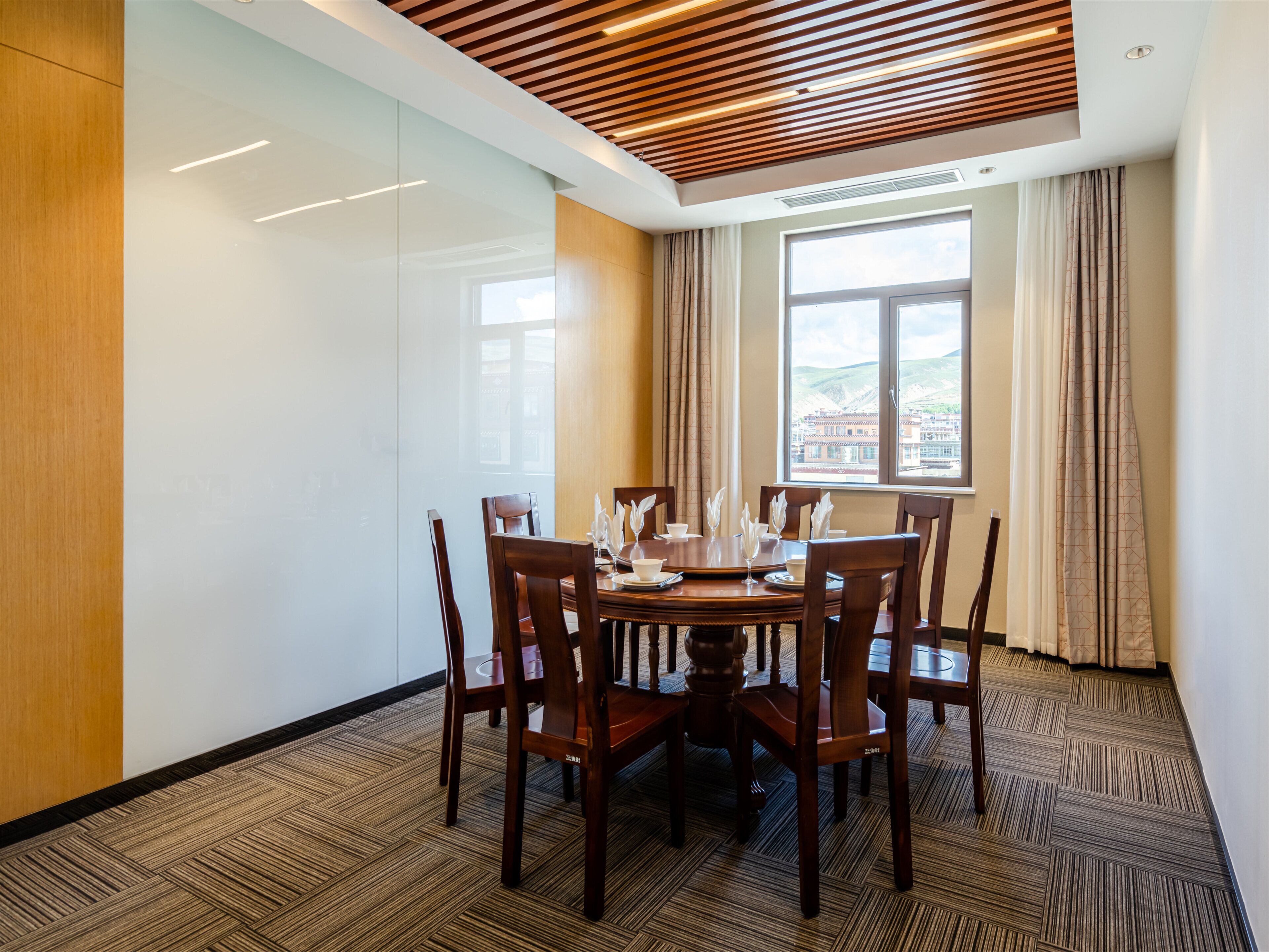 A conference room with a round table, wooden chairs, and a view of a cityscape through a large window.