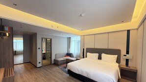 Ein modernes Hotelzimmer mit einem großen Bett, einer Sitzecke mit kleinem Tisch, einem Kleiderschrank und einem Spiegel.