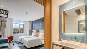 Ein Hotelzimmer mit zwei Betten, einem Schreibtisch mit Stuhl, einem Badezimmer mit Waschbecken und Spiegel sowie Blick ins Freie.