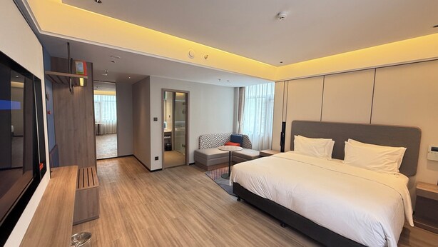 Ein modernes Hotelzimmer mit einem großen Bett, einem Fernseher, einem Schreibtisch und einer Sitzecke.