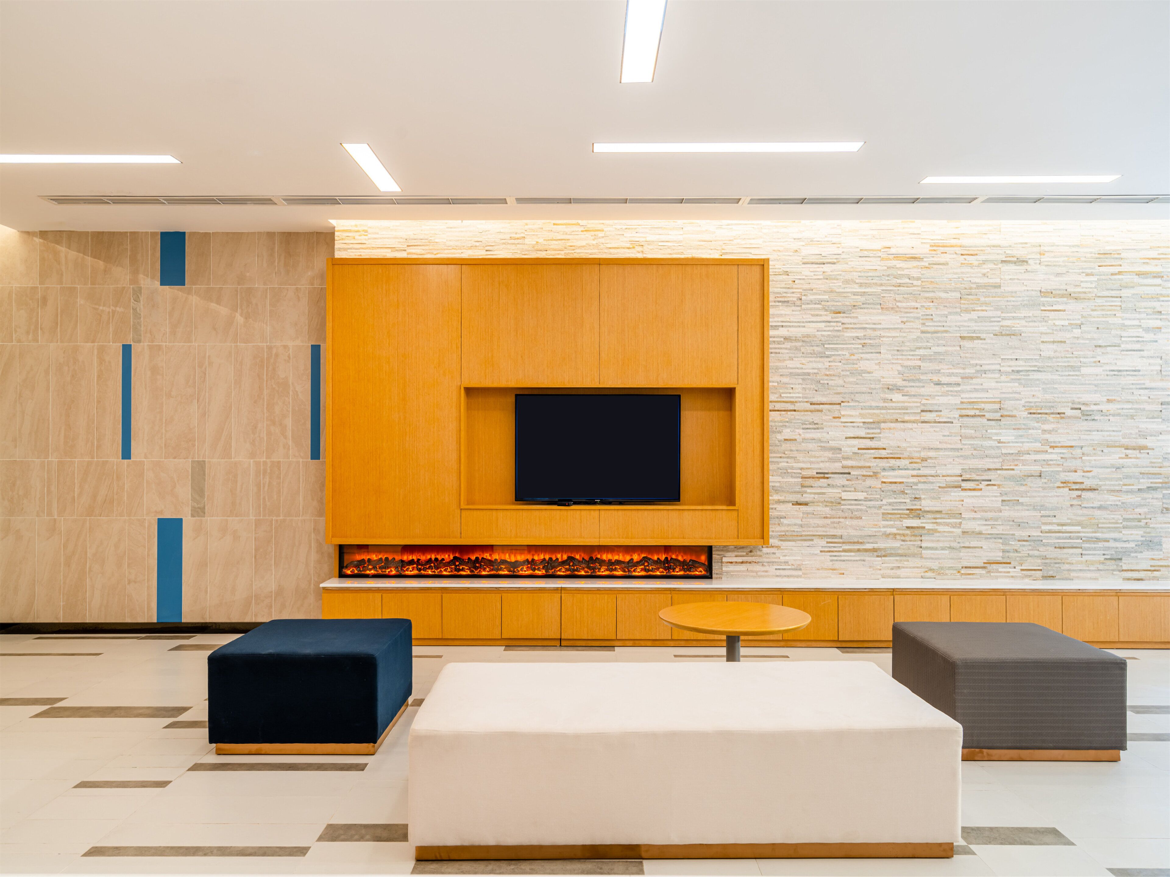 A modern interior with a flat-screen TV mounted on a wooden panel, a built-in fireplace, and three seating options.