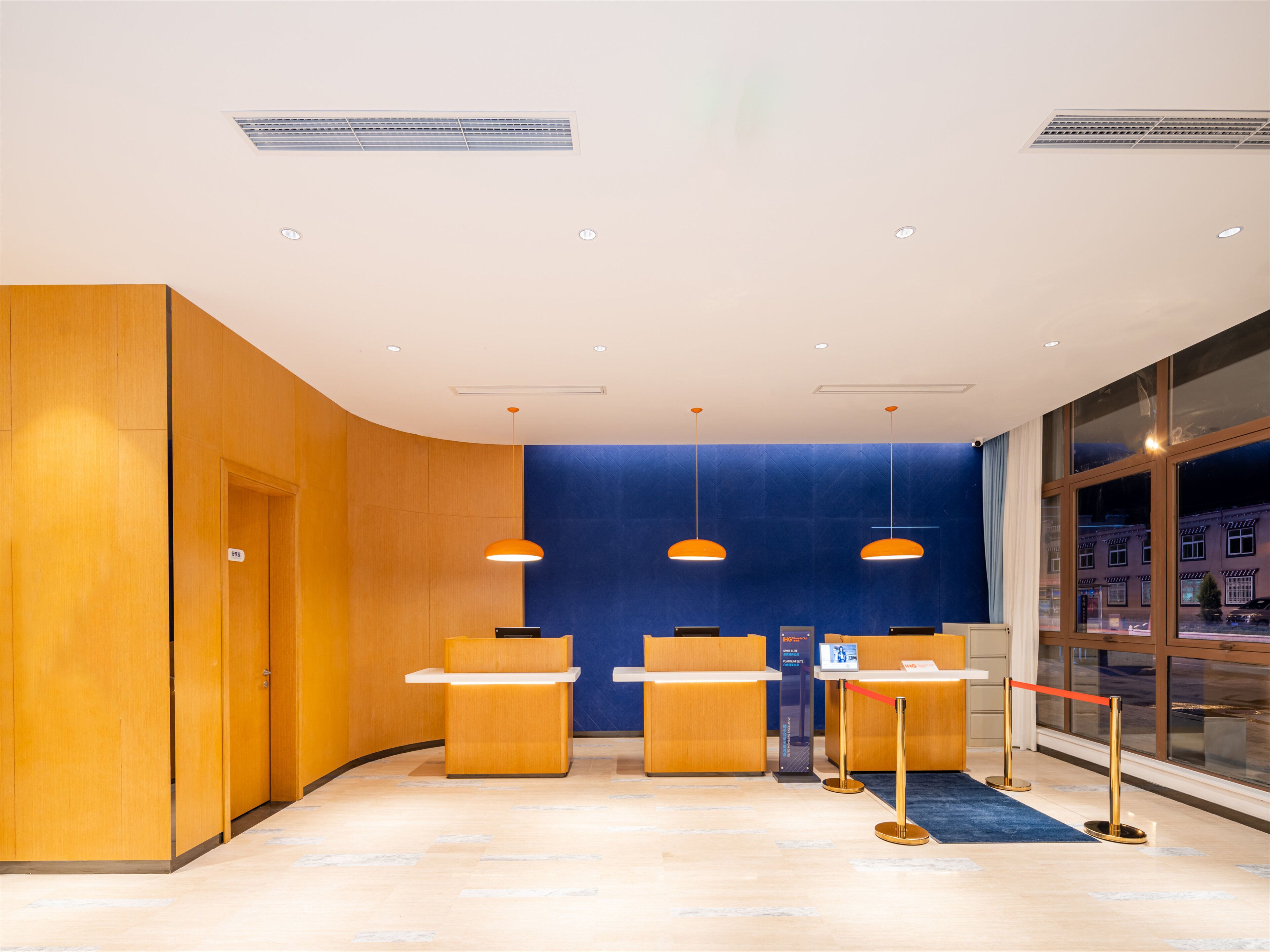 Un espace d’accueil doté de comptoirs de réception en bois, d’un mur d’accent bleu et de luminaires suspendus.
