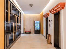 A hallway with a vending machine, a wooden floor, and an elevator.