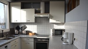 A modern kitchen with white cabinets, a stainless steel oven, a microwave, and a coffee maker. - Apartment at the port (Xanten)