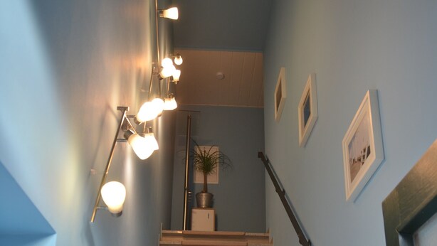 A staircase with beige steps and a handrail, leading to a landing with a light fixture and framed pictures on the walls. - Apartment at the port (Xanten)