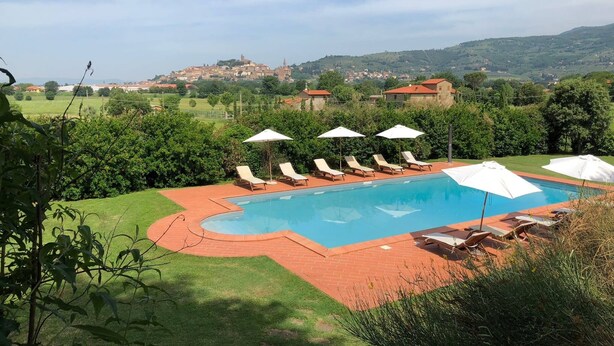 A swimming pool with lounge chairs and umbrellas, surrounded by greenery and a view of distant buildings. - Casa Legnaia, Tuscan Retreat in Castiglion Fiorentino (Castiglion Fiorentino)