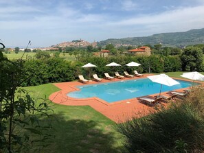 A swimming pool with lounge chairs and umbrellas, surrounded by greenery and a view of distant buildings. - Casa Legnaia, Tuscan Retreat in Castiglion Fiorentino (Castiglion Fiorentino)