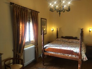 A bedroom with a wooden bed, a radiator, a chair, a window with curtains, and a chandelier. - Casa Legnaia, Tuscan Retreat in Castiglion Fiorentino (Castiglion Fiorentino)