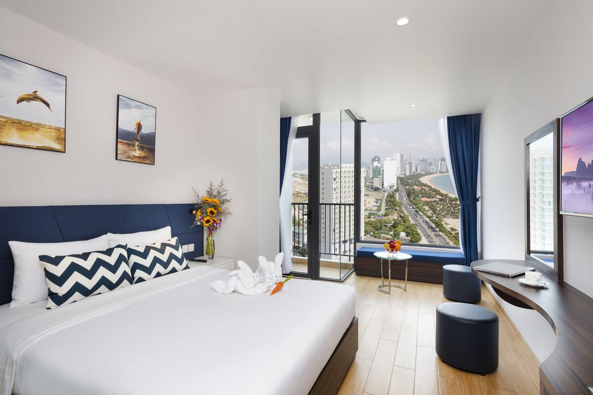 Une chambre d’hôtel moderne dotée d’un grand lit, d’un bureau et d’un balcon offrant une vue sur la ville.