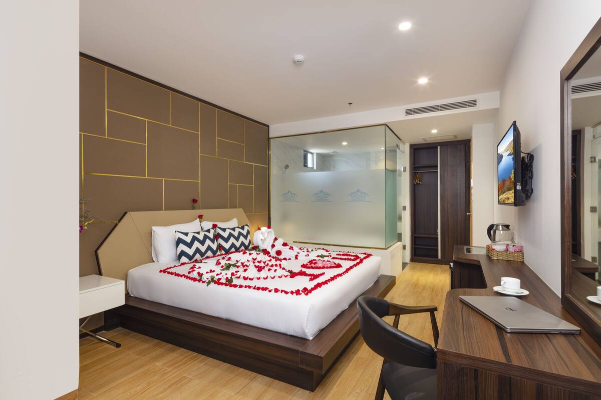 Une chambre d’hôtel moderne avec un lit bien fait, un bureau en bois, une chaise et un téléviseur fixé au mur.