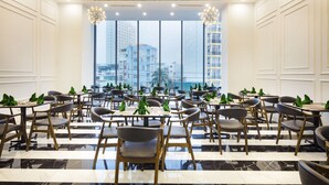 A spacious dining area with modern chairs and tables, large windows offering a city view, and decorative lighting fixtures. - Crown Hotel Nha Trang (Nha Trang)