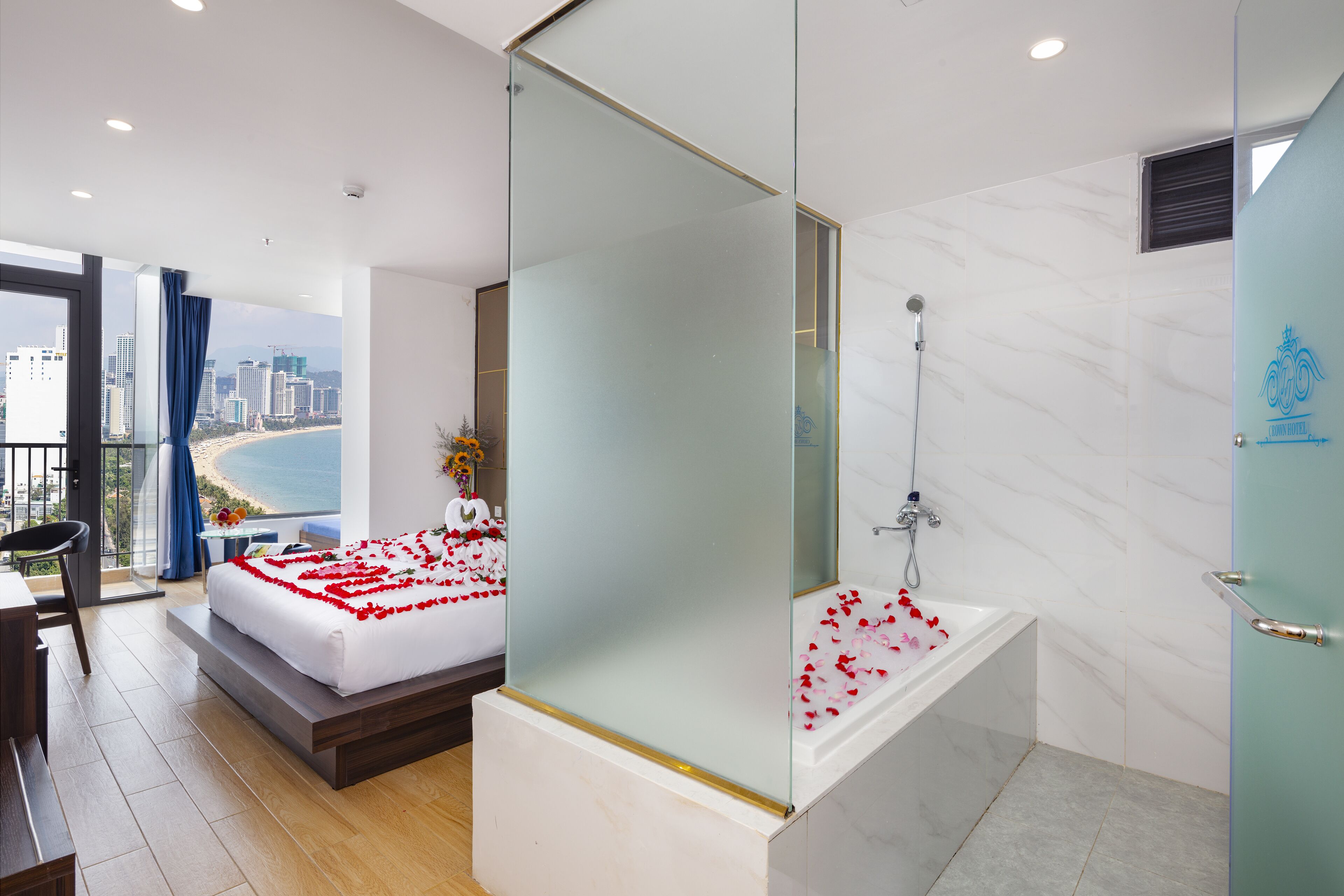 A modern hotel room with a balcony, a large bed, a glass-enclosed shower, and a view of the city.