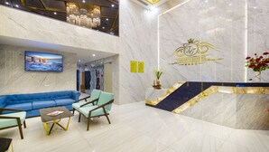 A hotel lobby with a marble reception desk, a blue sofa, and a television displaying a scenic view. - Crown Hotel Nha Trang (Nha Trang)