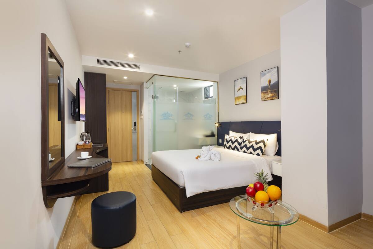 Une chambre d’hôtel moderne avec un lit, une table en verre sur laquelle se trouvent des fruits, un miroir et un téléviseur.