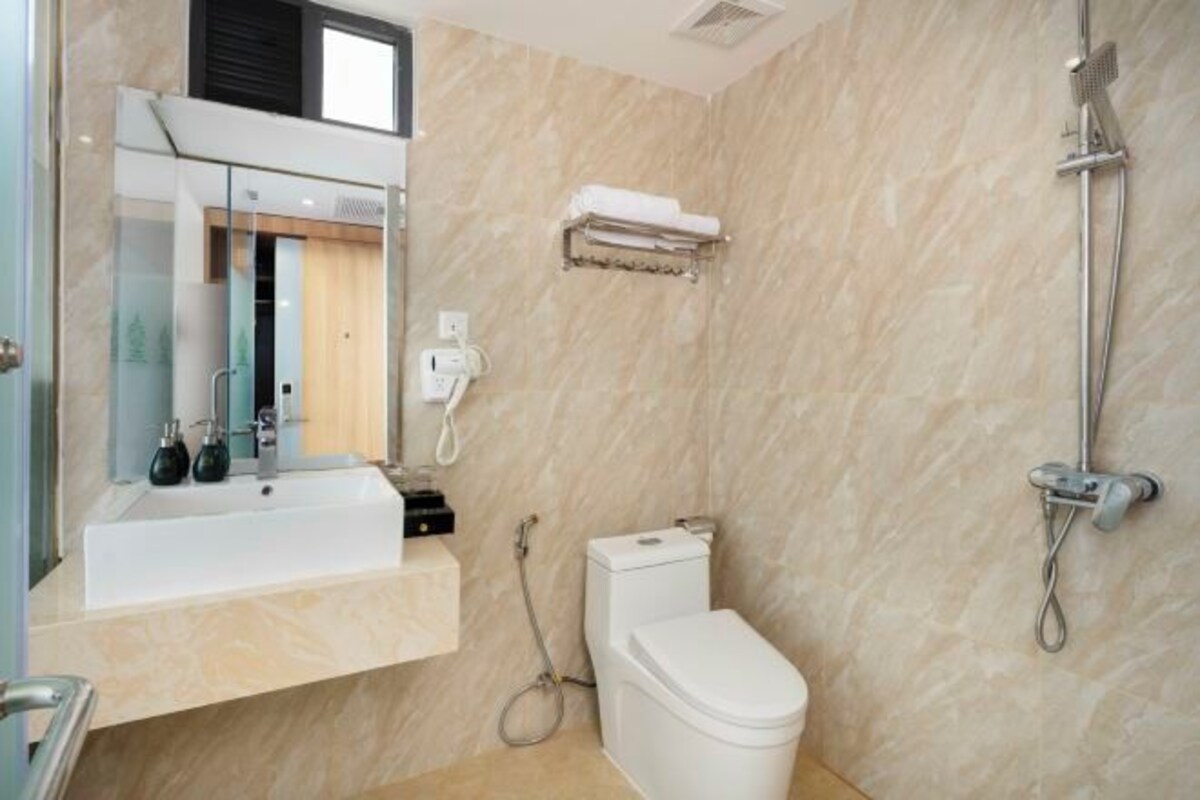 A bathroom with a white sink, mirror, and toilet. There is a towel rack above the toilet and a showerhead on the right.