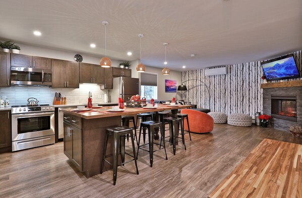A modern kitchen with stainless steel appliances, a wooden island with bar stools, and a fireplace.
