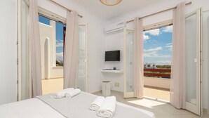 A hotel room with a bed, a television, and a balcony with curtains. - Rocks Naxian Villa, private Pool, by NaxosVibe (AGIA ANNA, NAXOS)