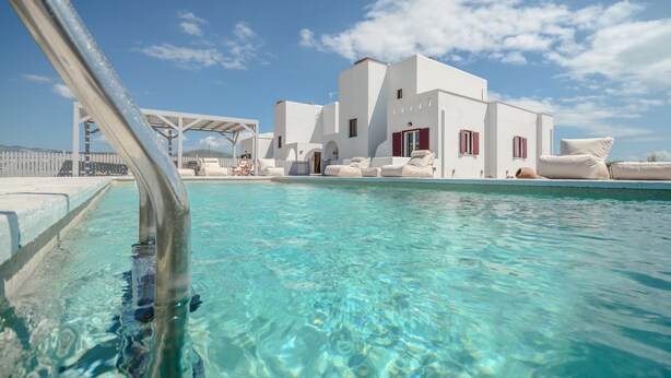 A clear pool with a white building in the background, a pergola, and lounge chairs. - Rocks Naxian Villa, private Pool, by NaxosVibe (AGIA ANNA, NAXOS)