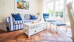 A sunlit room with a striped sofa, a lounge chair, and a large window. - House Moin Munkmarsch (Sylt-Ost)