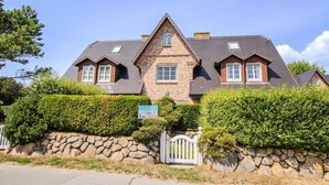 A two-story house with a stone wall, a wooden fence, and a clear blue sky. - House Moin Munkmarsch (Sylt-Ost)