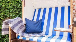 A striped outdoor lounge chair with a cushion, a small table with a book, and a blanket. - House Moin Munkmarsch (Sylt-Ost)