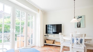 A bright room with a TV, white furniture, and a large window. - House Moin Munkmarsch (Sylt-Ost)