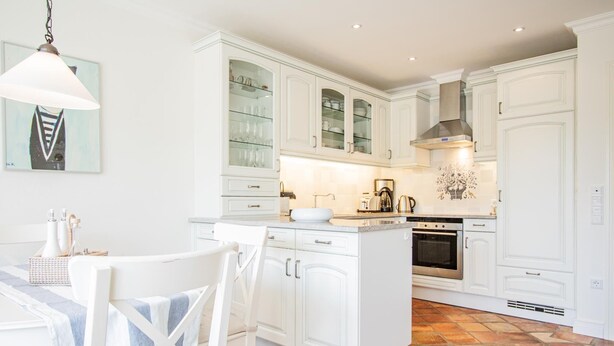 A modern kitchen with white cabinetry, a central island, and a dining area with white chairs. - House Moin Munkmarsch (Sylt-Ost)