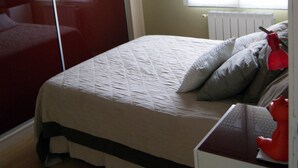 Una camera da letto con un letto, una finestra con persiane, un termosifone e un giocattolo rosso su un comò.