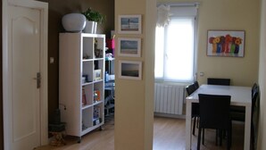 Un soggiorno con un divano, un tavolo da pranzo con sedie, una libreria bianca e un termosifone.