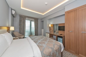 A hotel room with a large bed, a desk, a chair, a wardrobe, and a television. - Floransa City Hotel (Istanbul)