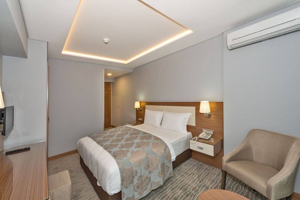 A hotel room with a bed, bedside lamps, a chair, a desk, and a television.
