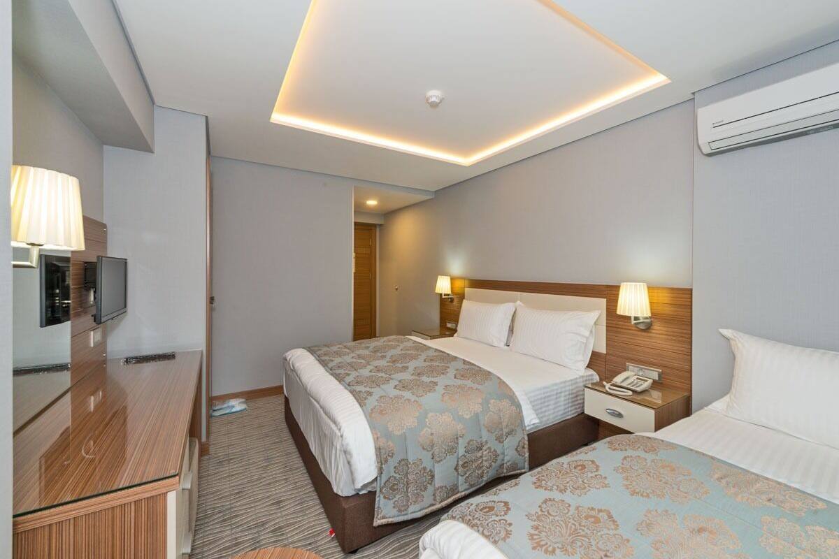 A hotel room with two beds, a desk, a TV, and a ceiling light.