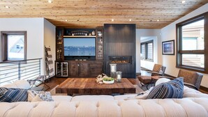 A modern living room with a wooden ceiling, a fireplace, a large TV, and a cozy seating area. - Lake View Home with Private Hot Tub (Tahoma)