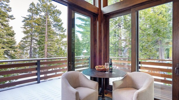 A balcony with two chairs, a table, and a view of tall trees. - Lake View Home with Private Hot Tub (Tahoma)