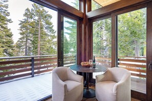 A balcony with two chairs, a table, and a view of tall trees. - Lake Views with Private Hot Tub (Tahoma)
